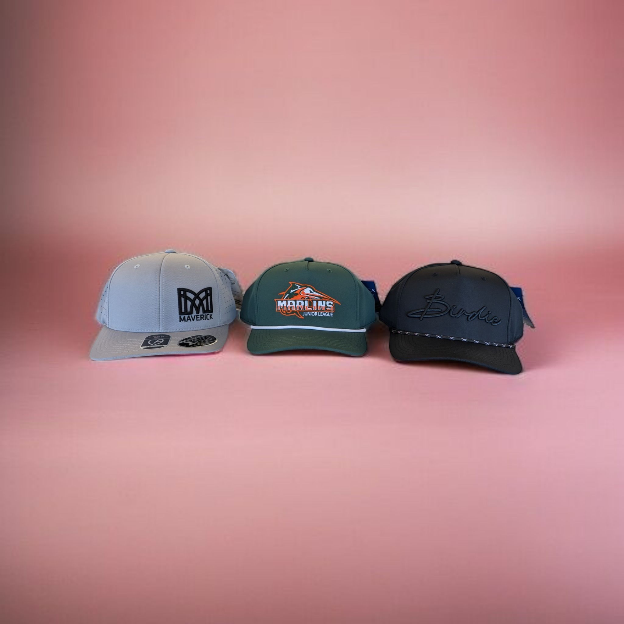 Three embroidered caps side by side — a structured trucker, a mesh youth-sports cap, and a rope-brim golf-style cap